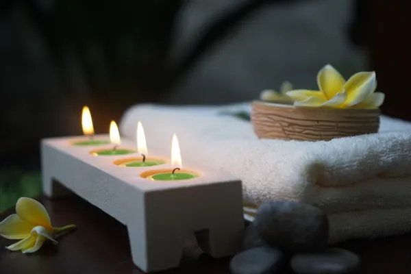 Illustrative stock photograph of glowing candles, folded spa towels and flowers