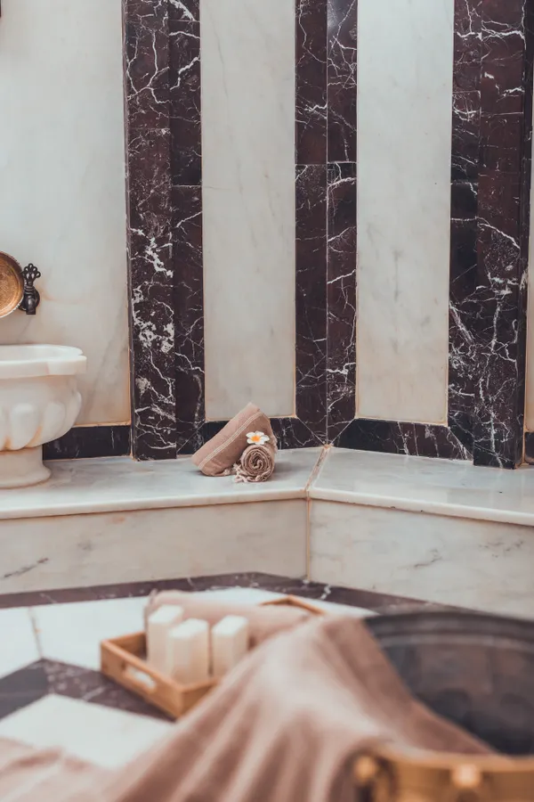Illustrative stock photograph of a marble hammam with a brass bathing bowl, candles and soft towels