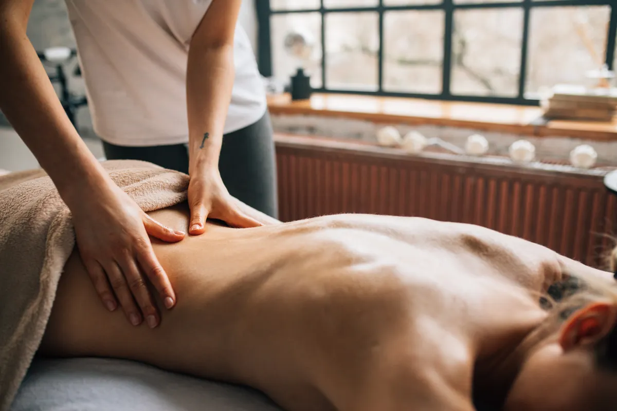 Illustrative stock photograph of a professional back massage with soft towels in a warm, naturally lit treatment room